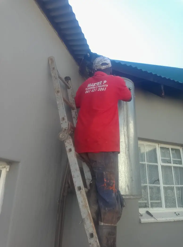 Plumber installing an electric geyser on an exterior wall